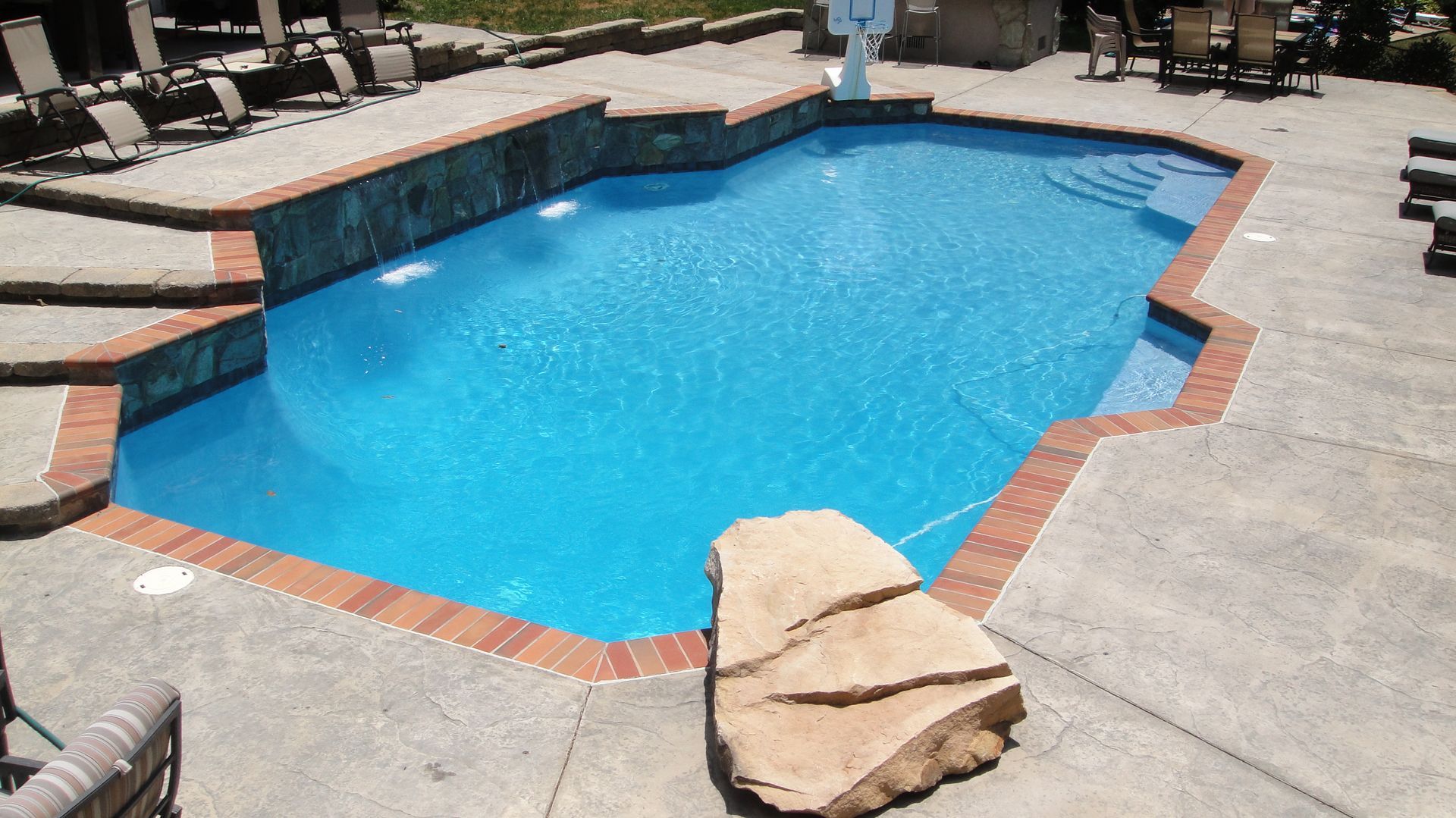 Pool with blue water and brick border on a concrete patio.