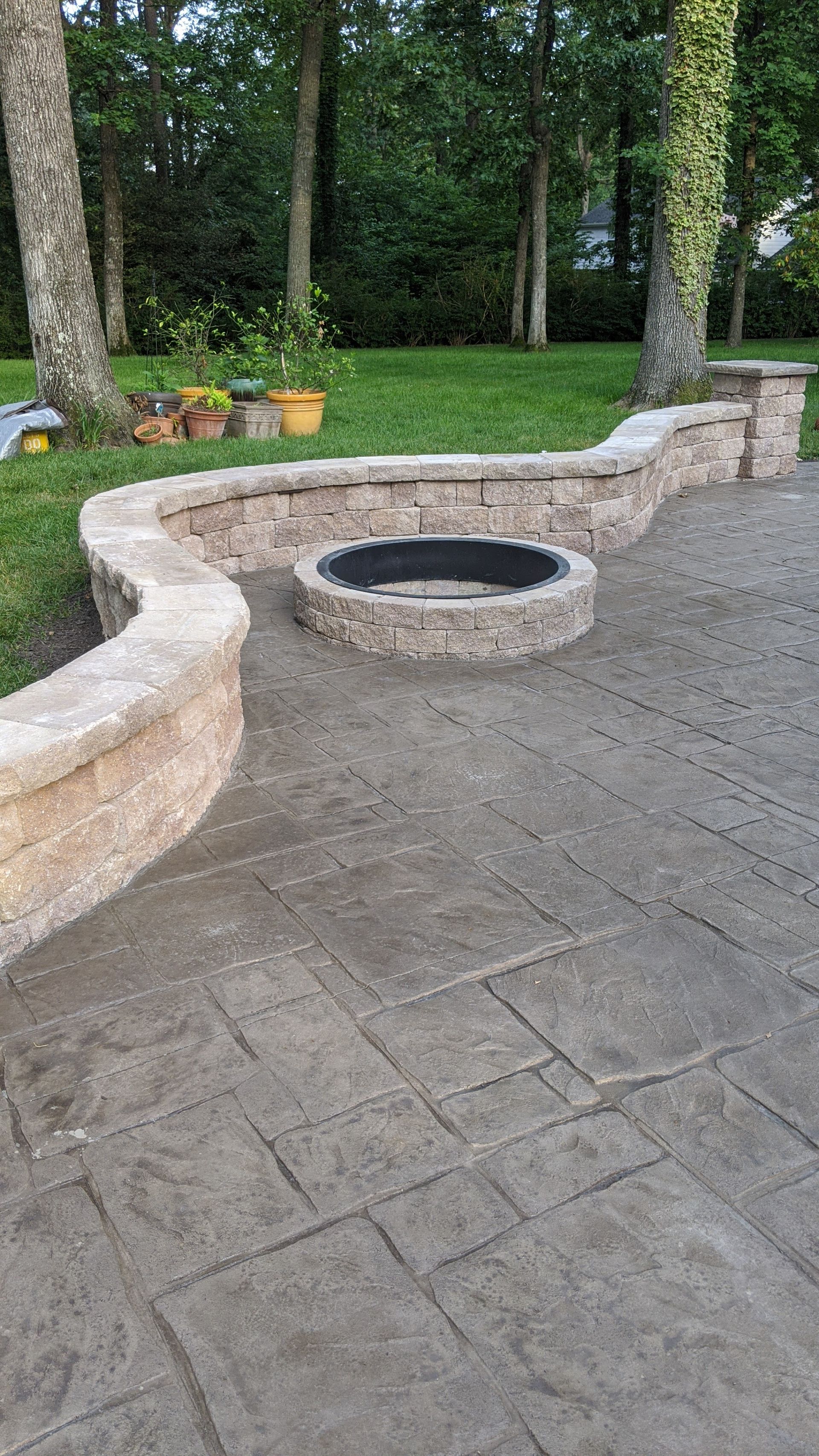 Stone patio with curved retaining wall and fire pit in a grassy backyard.