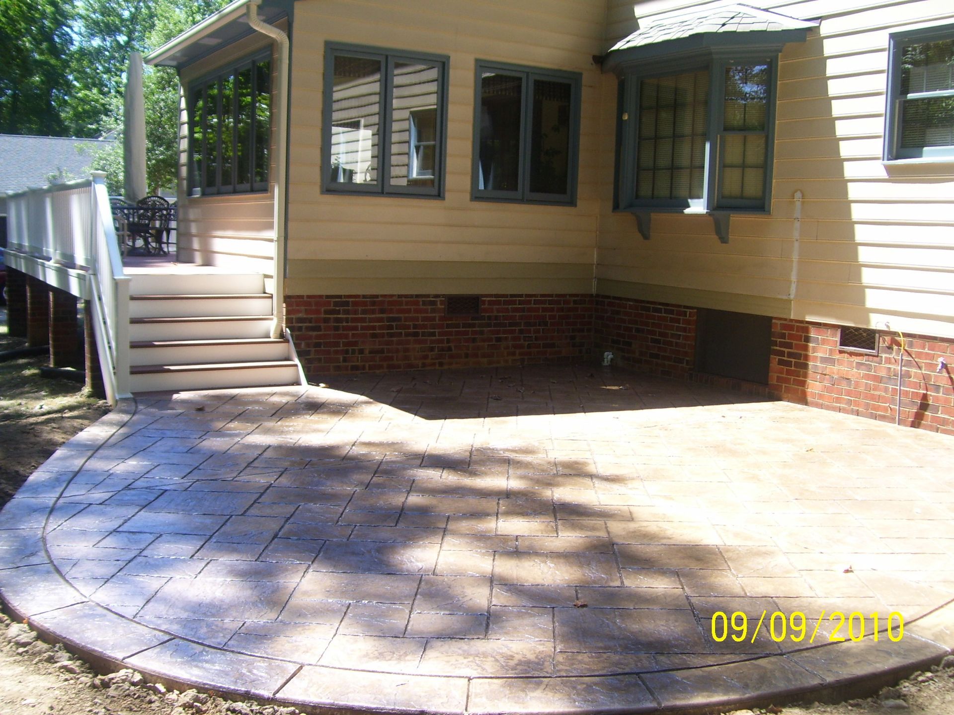 Brick patio with curved edge next to a house with steps and windows.