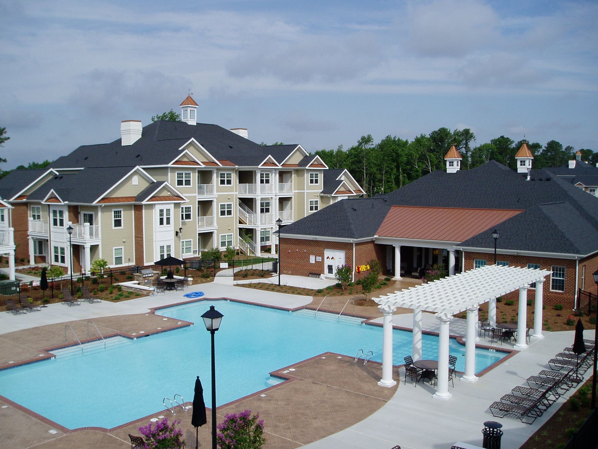 Apartment complex with a pool, brick buildings, and white pergola.