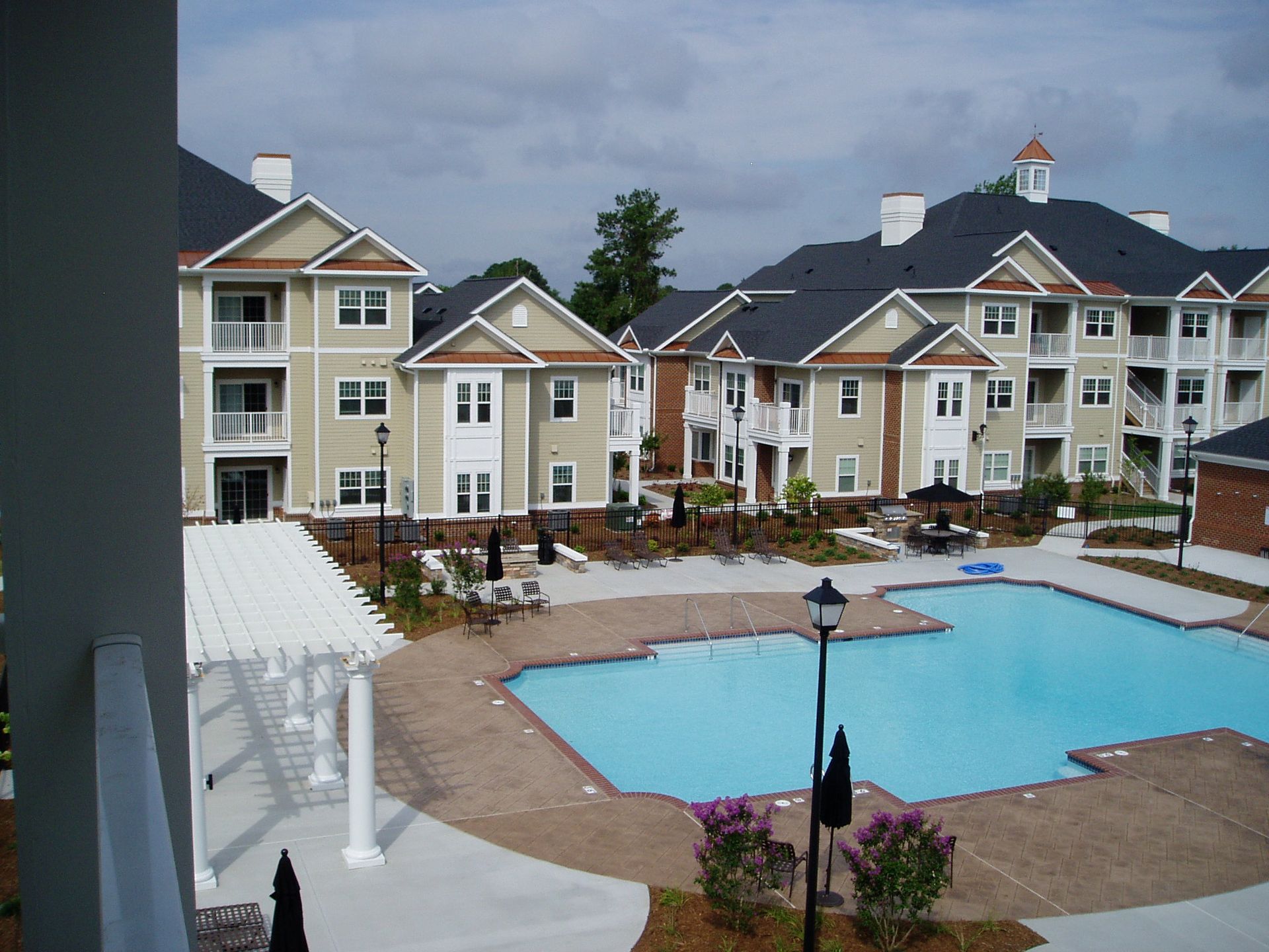 Apartment complex with a pool. Buildings are tan with black roofs.