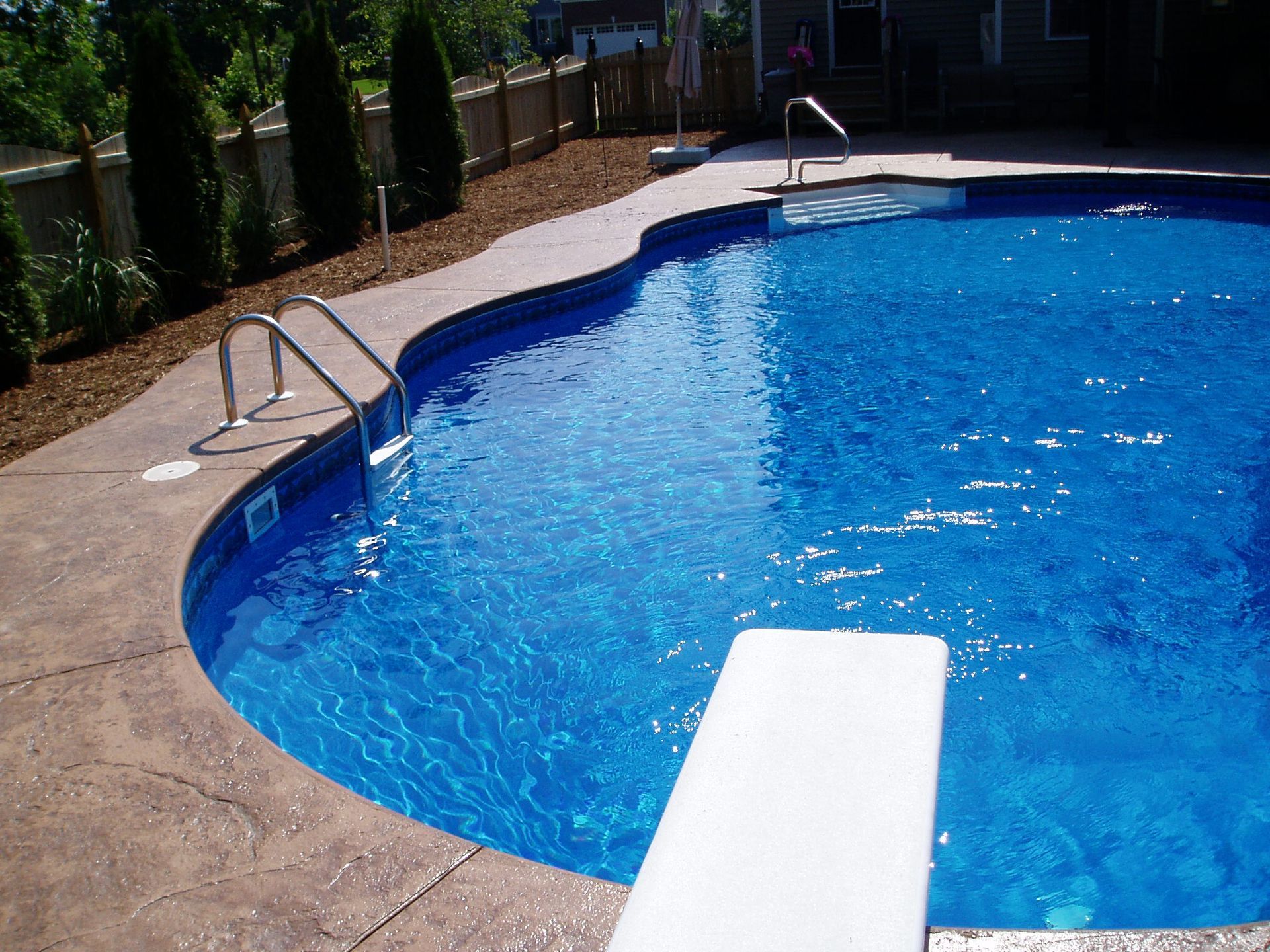 Swimming pool with a diving board, concrete border, and blue water.