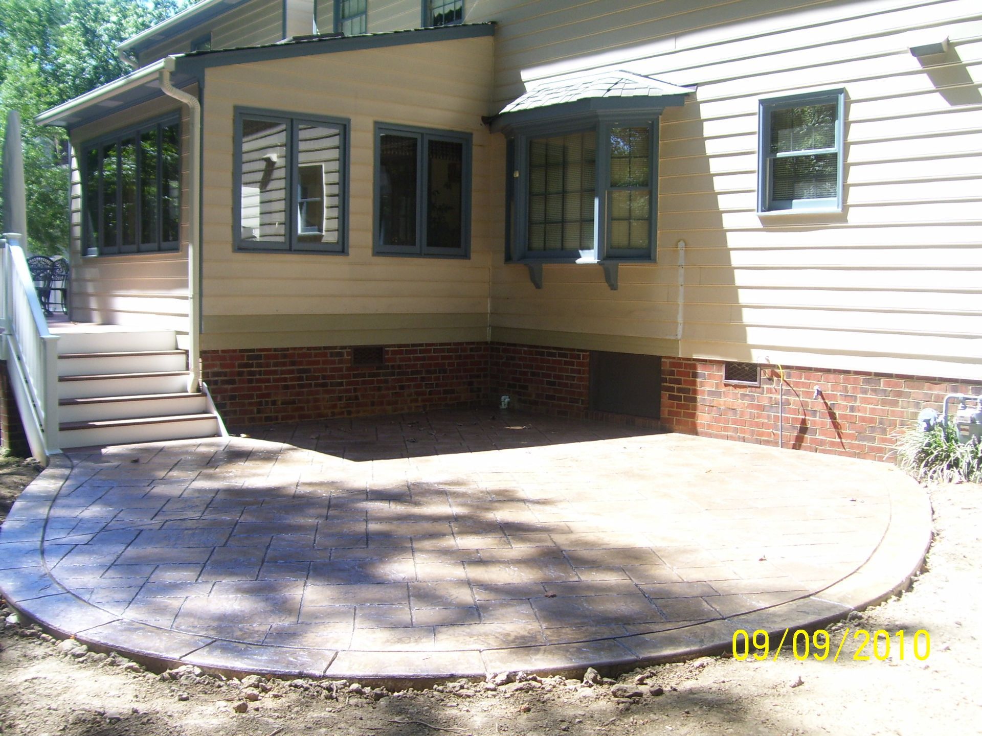Backyard patio with brick foundation, beige siding, and multiple windows.
