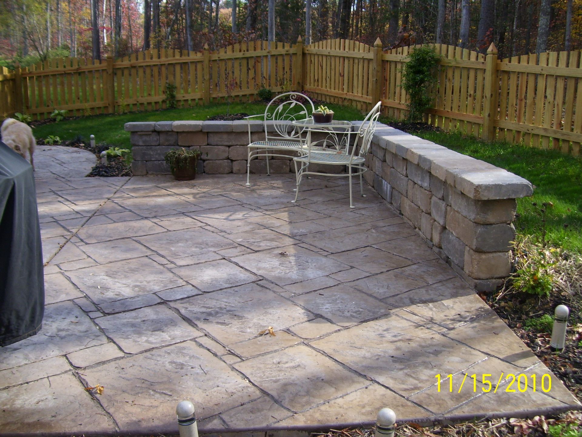 Patio with stone pavers, low wall, wrought iron furniture, wooden fence, and trees.