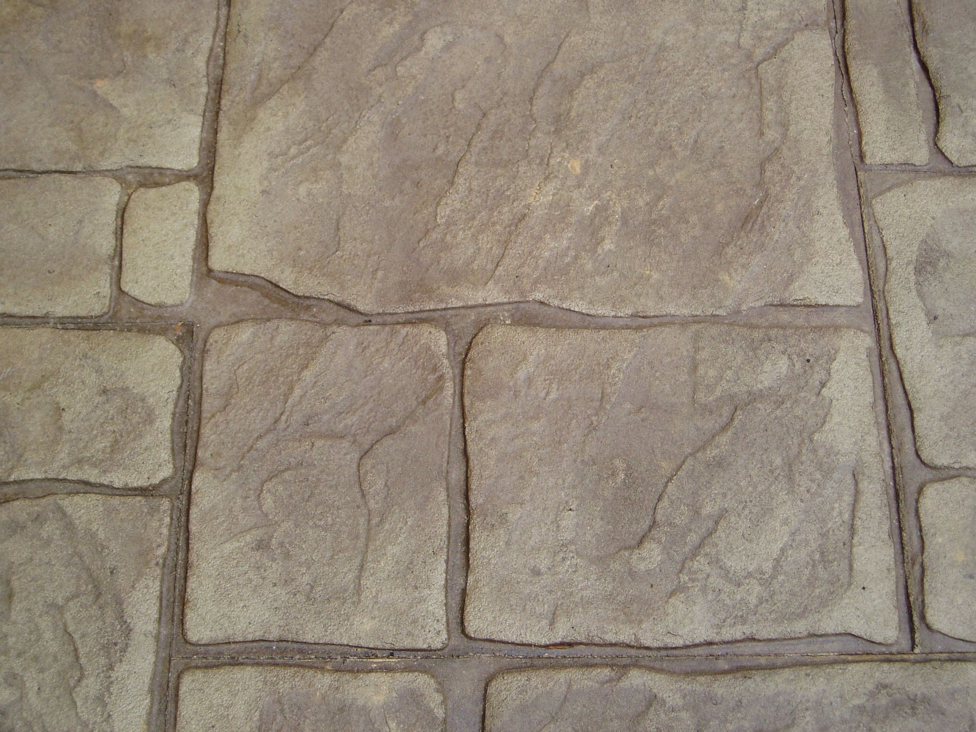 Textured, light-brown concrete paving, stamped to resemble large, irregular stone blocks with dark grout lines.