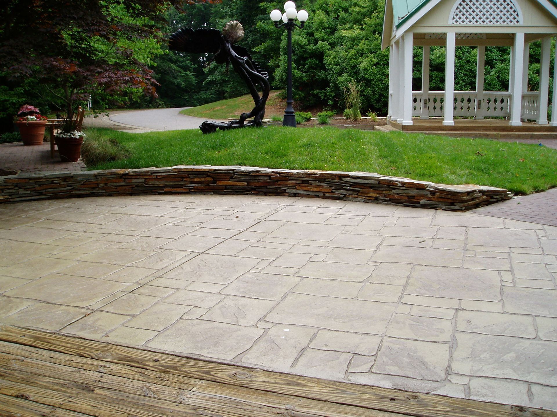 Patio with stone pavers, a low stone wall, and gazebo on a grassy area.