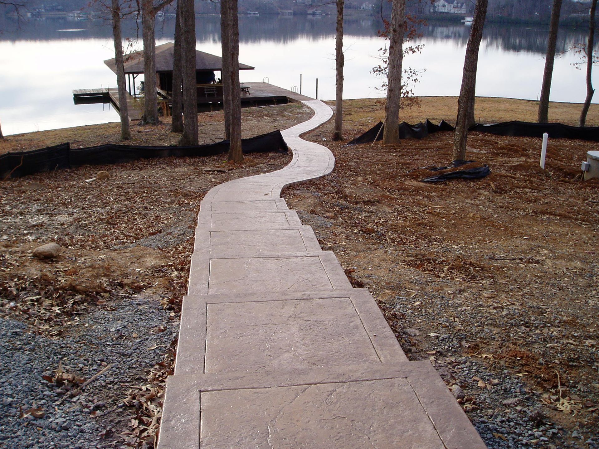 Concrete pathway leading to a dock on a lake, passing through trees.