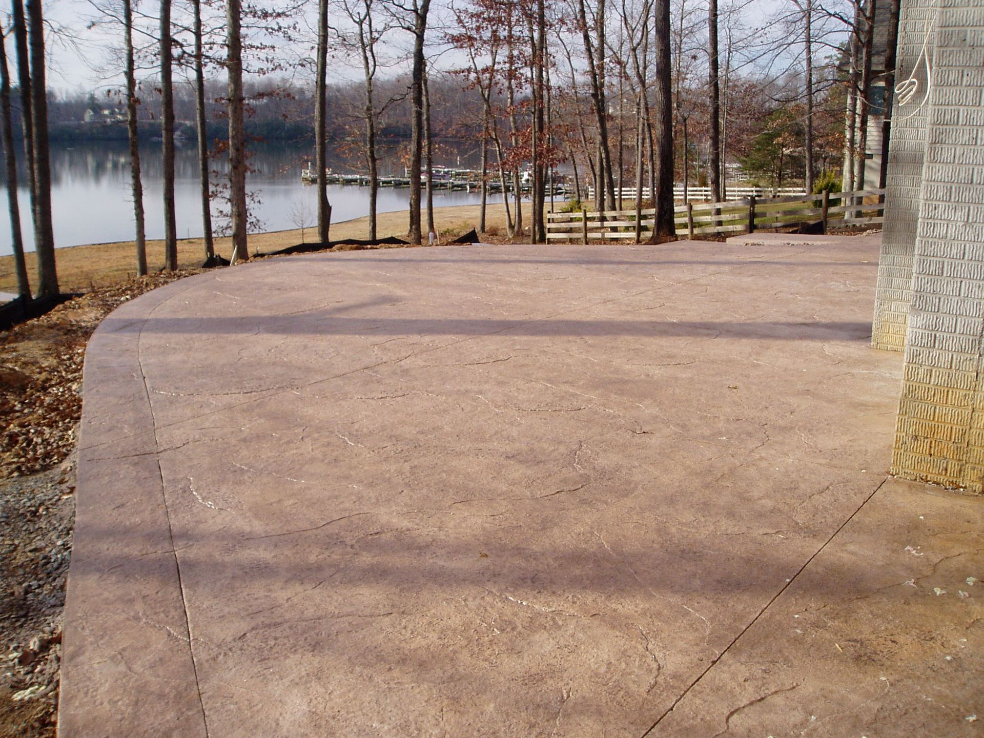 Brown concrete patio beside a lake with trees.