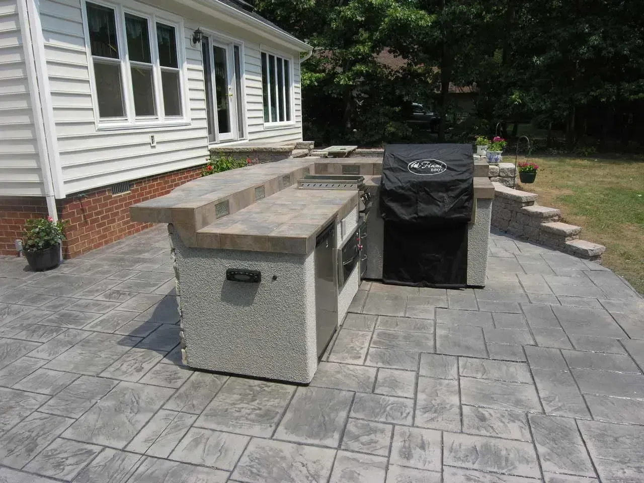 Outdoor kitchen with concrete countertops and grill on a patio.