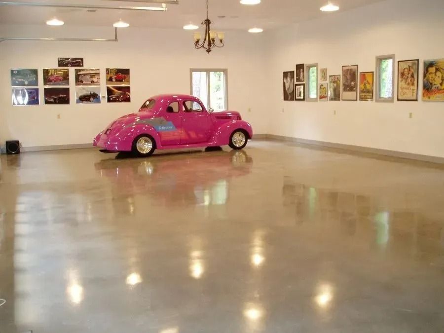 Pink car in a large, polished concrete garage with movie posters on the wall.