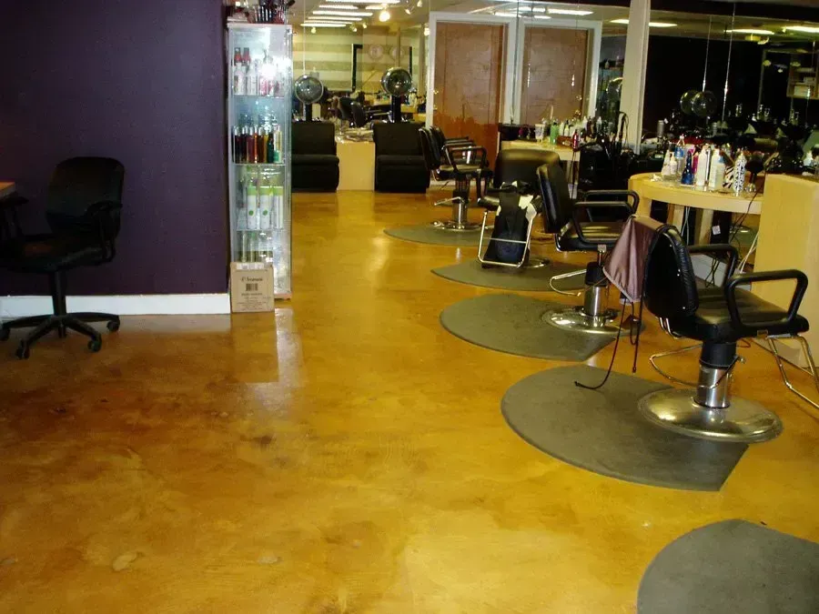 Salon interior with gold-toned floor, purple wall, black chairs, and hair styling stations.