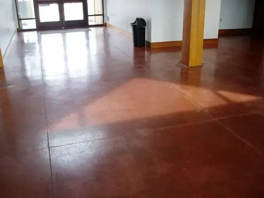 Brown stained concrete floor, sunlight, dark trash can, and wooden structural pillar.