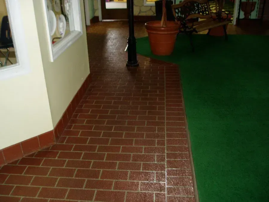 Brick-patterned flooring transitions to green carpet. A large flower pot, bench, and lamppost are nearby.