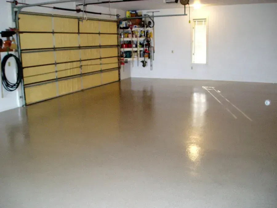 An empty, light beige garage with a glossy floor, closed garage door, shelves of tools, and a small window.