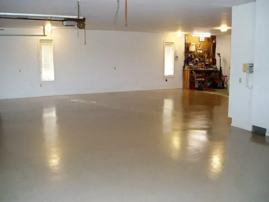 Empty garage with glossy, tan-colored floor and white walls; a workbench is in the back.