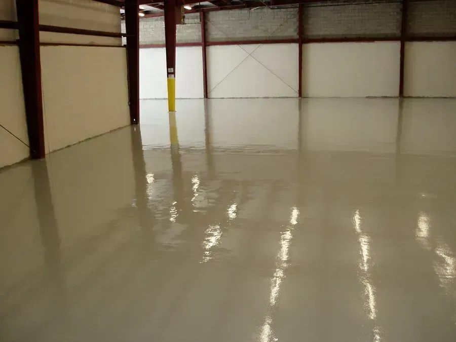 Interior view of a warehouse with a shiny, light-colored epoxy floor, and steel beams.