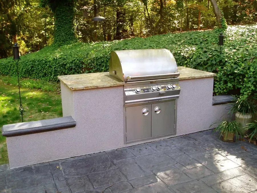 Outdoor built-in grill with stainless steel features, granite countertop, and concrete base in a backyard setting.