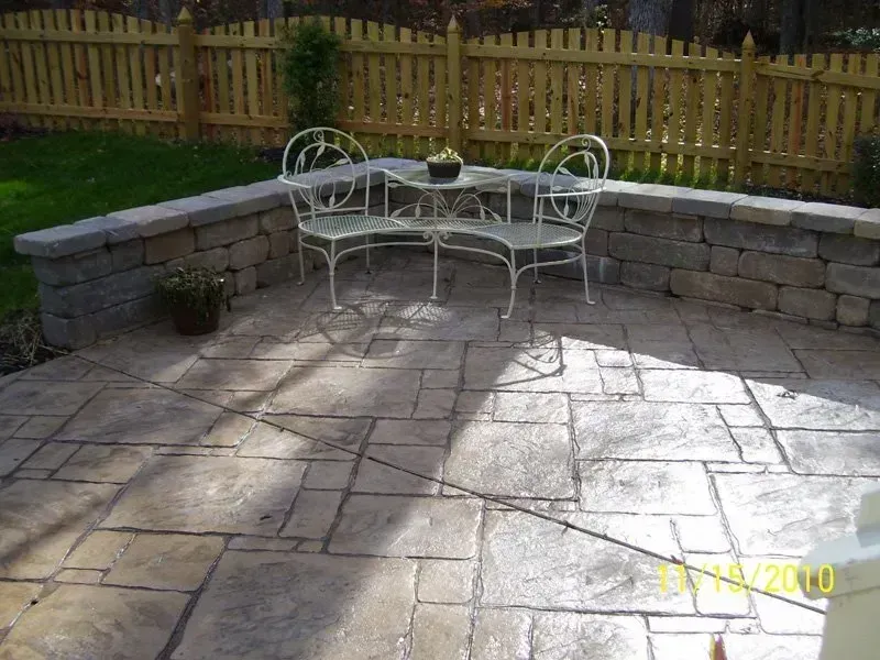Patio with stone wall, concrete pavers, and white metal bistro set. Wooden fence in background.