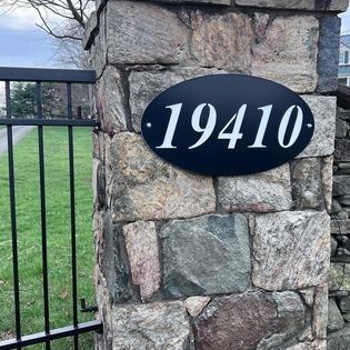 A black sign on a stone wall with the number 19410 on it.