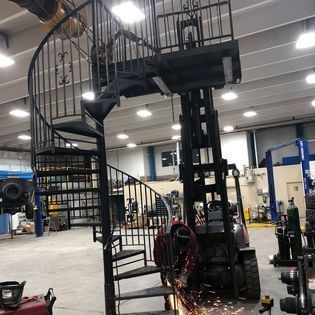 A forklift is cutting a piece of metal next to a spiral staircase
