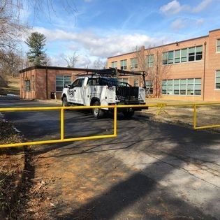 A white truck is parked in front of a brick building next to a yellow fence.