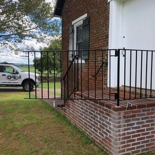 A white truck is parked in front of a brick building with a wrought iron railing.