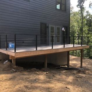 A wooden deck with a metal railing is in front of a house.