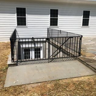 A white house with a black fence around a basement window.