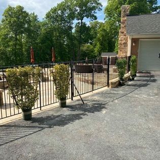 A driveway with a fence and potted plants in front of a house.