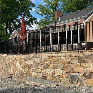 A stone wall with a fence around it and a house in the background.