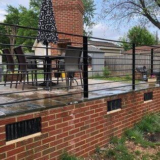 A brick wall with a metal railing and a table and chairs on it.