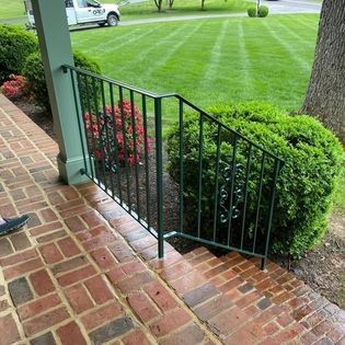 A person is standing on a brick sidewalk next to a green railing.