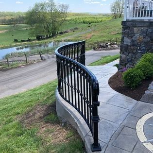 A wrought iron fence surrounds a concrete walkway with a view of a river.