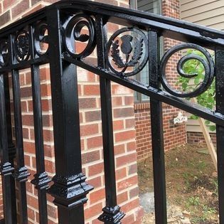 A black wrought iron railing is sitting in front of a brick building.