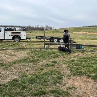 A man is working on a fence in a field next to a truck.