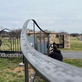 A man is working on a wrought iron gate in a field.