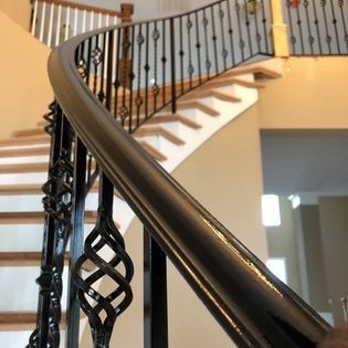 A close up of a curved staircase with a wrought iron railing.