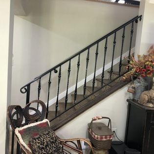 A staircase with a wrought iron railing and a wicker chair in a living room.