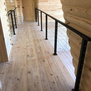 A wooden hallway with a black railing in a log cabin.