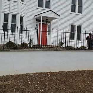 A white house with a red door behind a wrought iron fence