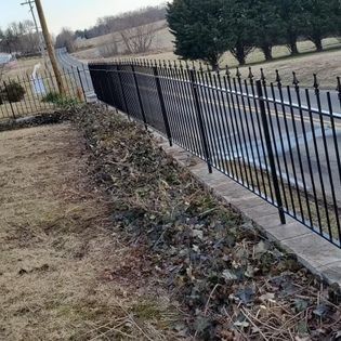 A black wrought iron fence surrounds a lush green field.