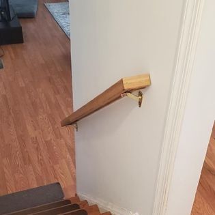 A wooden handrail is attached to a wall next to a set of stairs.