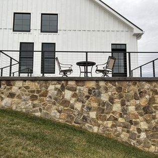 A white house with a stone wall and a balcony with chairs and a table.