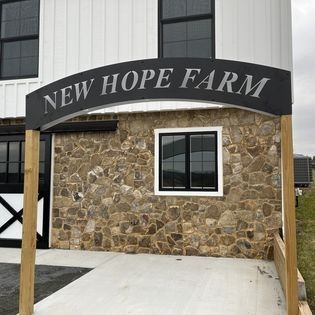 A sign for new hope farm is above a stone building.