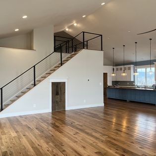 A large empty room with hardwood floors and stairs leading up to the second floor.