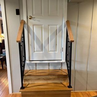 A wooden staircase leading up to a white door with a black railing.
