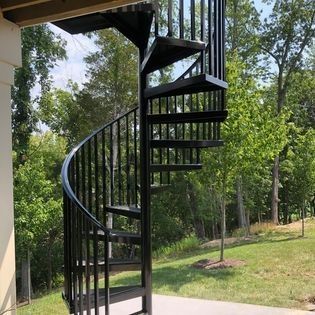 A black spiral staircase is surrounded by trees and grass.