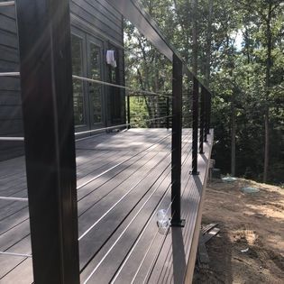 A wooden deck with a black railing and trees in the background.