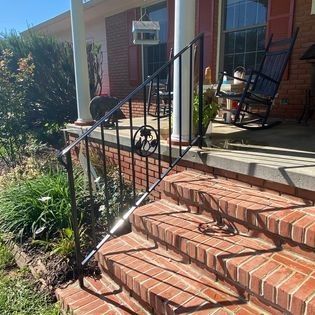 A brick porch with a wrought iron railing and a rocking chair.