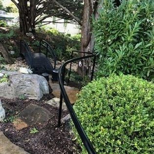 A black railing is surrounded by trees and bushes in a garden.